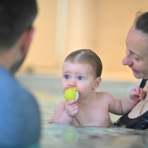 Bébé dans les bras de sa maman dans la piscine en train de mordre un jouet