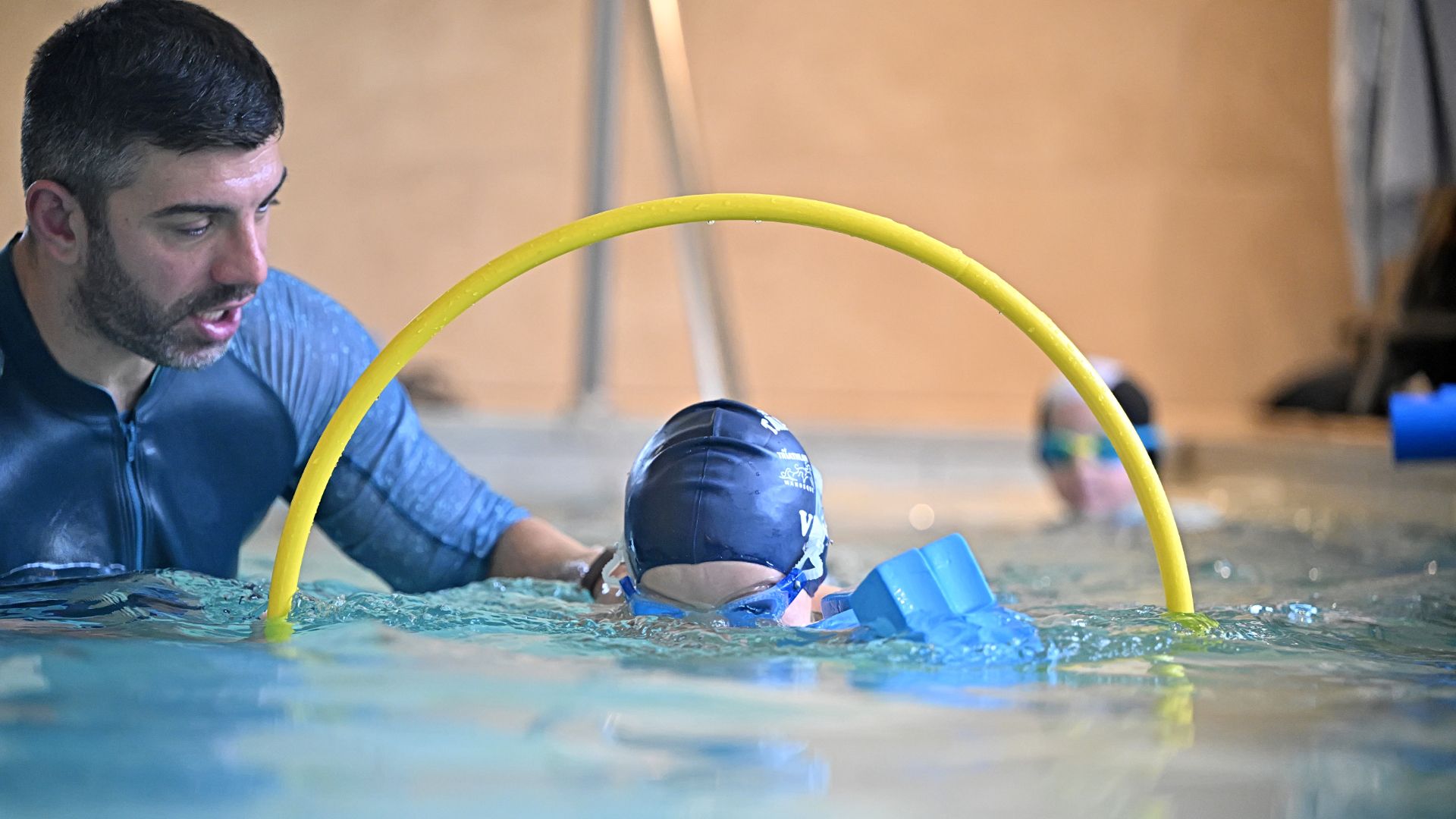 Enfant npassant en nageant dans un cerceau aux côtés du maître nageur